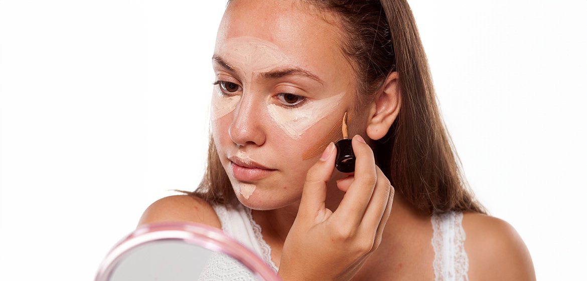 Junge Frau trägt Concealer als Highlighter auf Stirn, Nase, Kinn und Amorbogen auf.